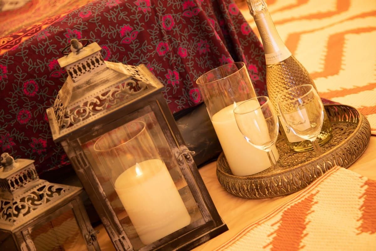 Lit candles in a glamping tent with a bottle of wine and two glasses on a tray