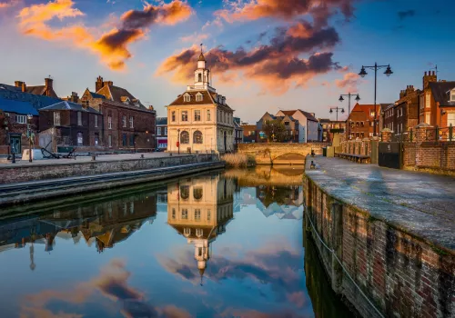 the customs house in King's Lynn reflected in the water below it, the sun setting in the background with pink and blue clouds