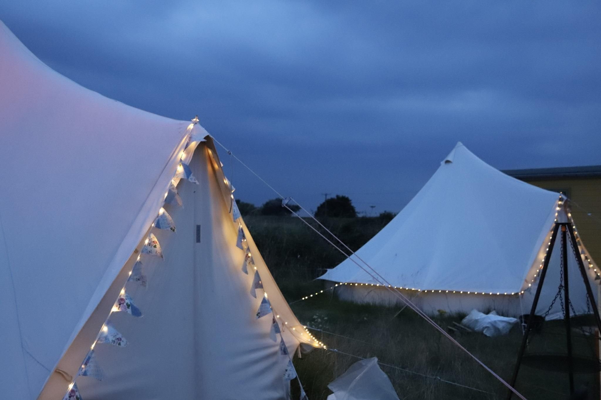Two bell tents lit up with fairy lights at dusk