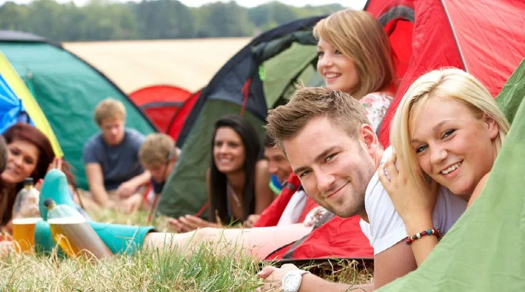 a group or party booking of young adults socialising outside their tents in a field