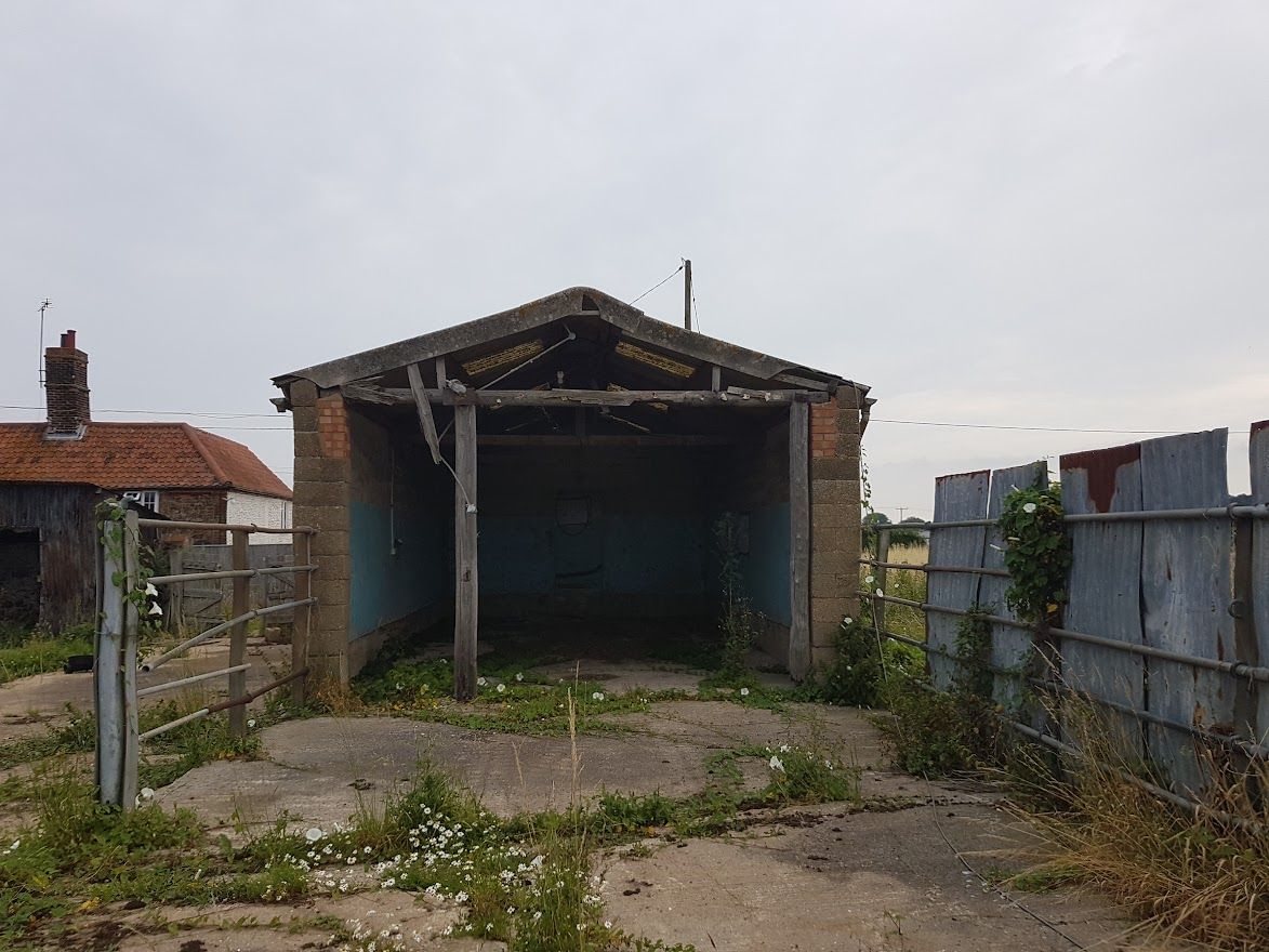 a lonely, dilapidated cowshed with cracked concrete and weeds growing inside