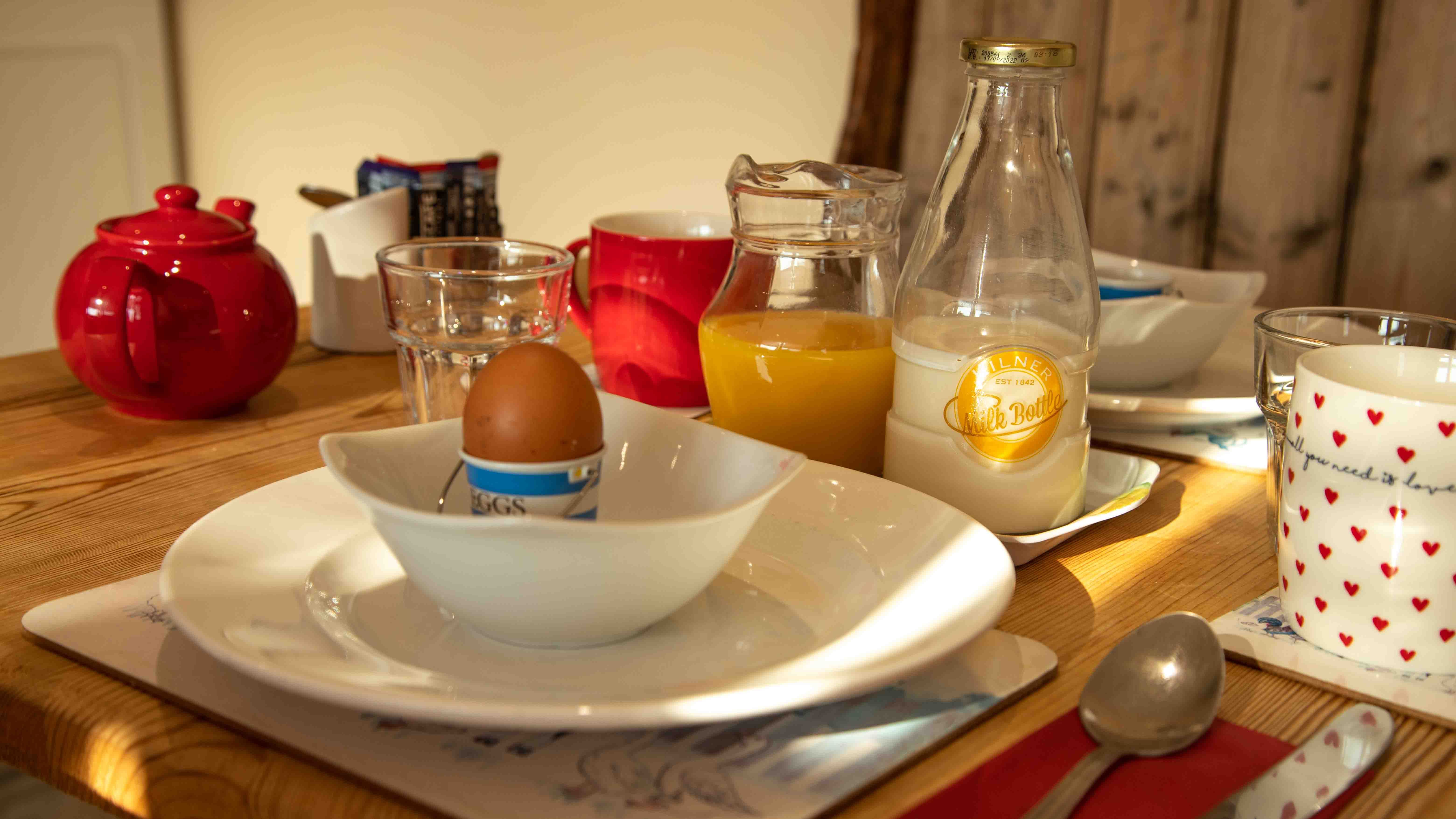 a table set with cutlery, crockery, milk, juice, eggs, and other breakfast items